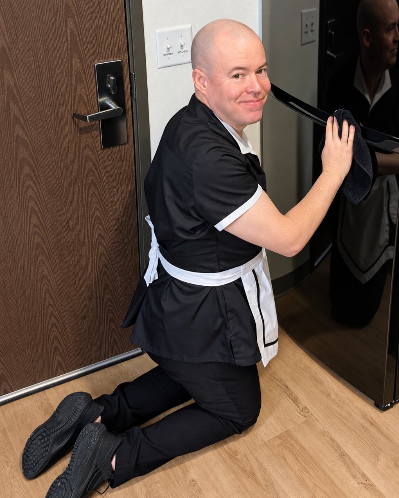 Maid Ray Berry kneeling in uniform, wiping down a refrigerator door with a microfiber cloth