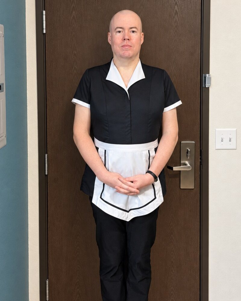 Maid Ray Berry in the working uniform: black housekeeping tunic, white piped apron, black trousers
